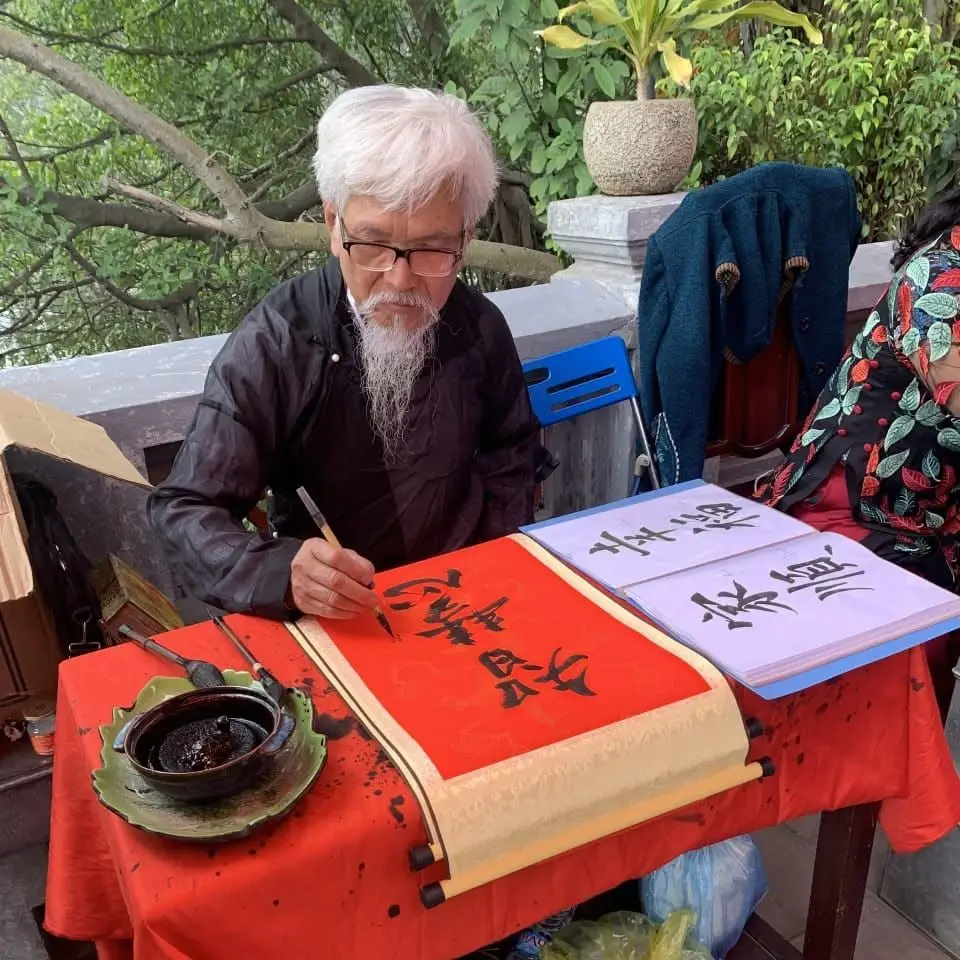Traditional Vietnamese calligraphy master writing brush calligraphy on red paper.